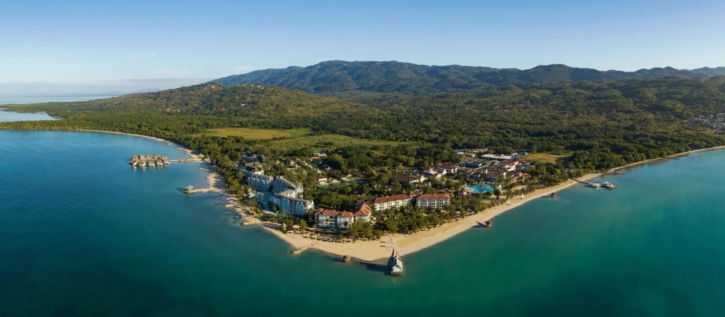 Panoramic aerial of Sandals South Coast on a peninsula with mountains beyond.