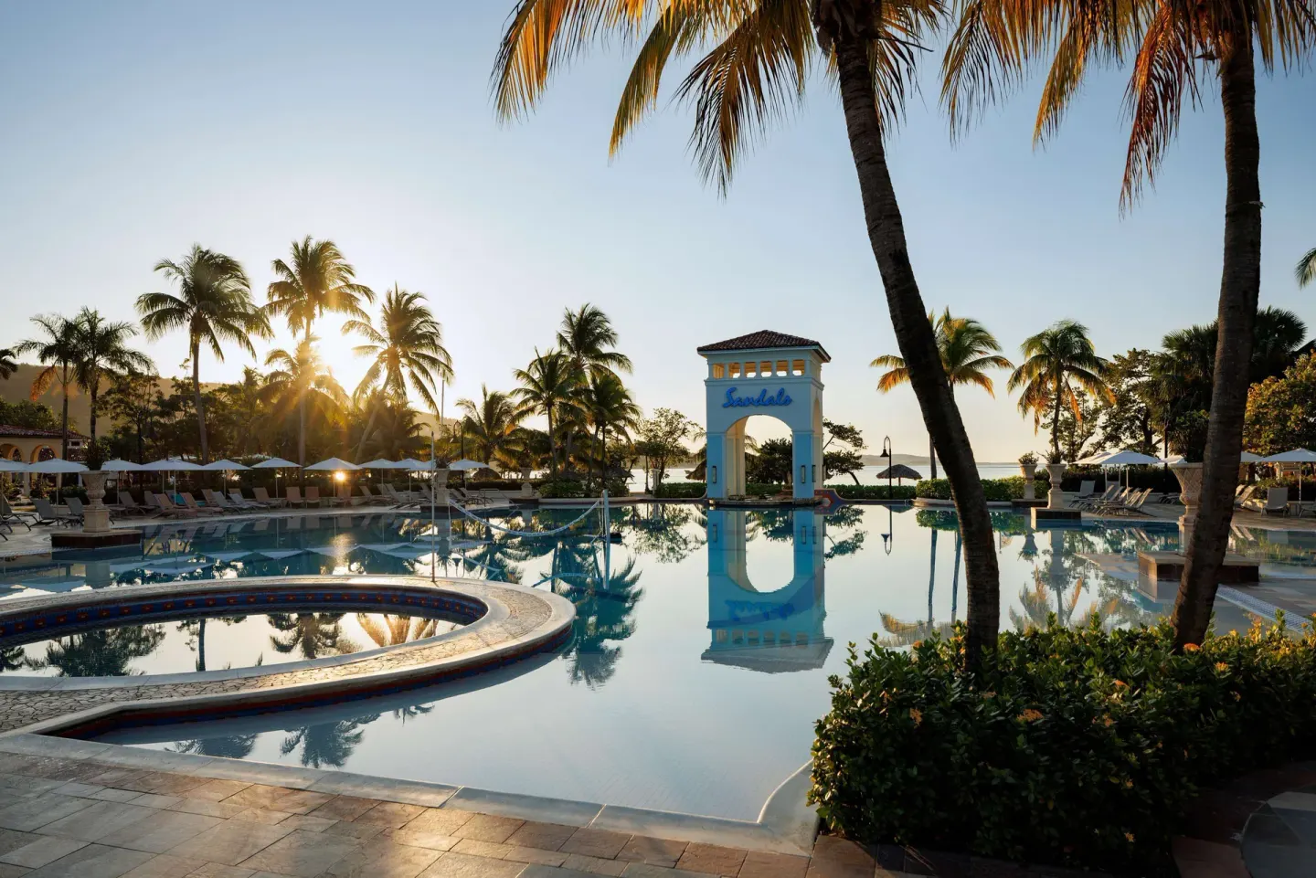 Sunlit main pool with palm trees and arch at Sandals South Coast.