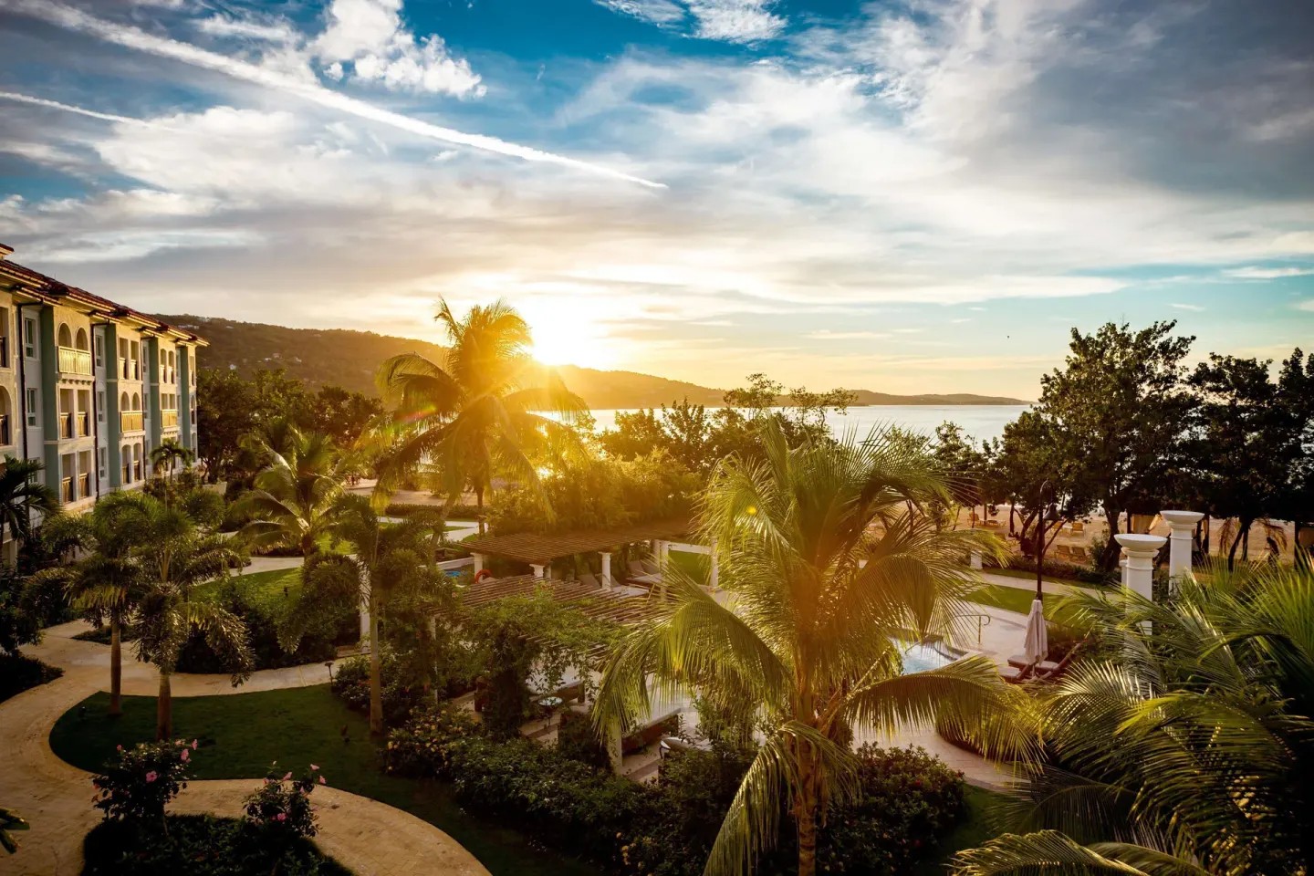 Sunset over palms, gardens, a pool area, and shoreline at Sandals South Coast.