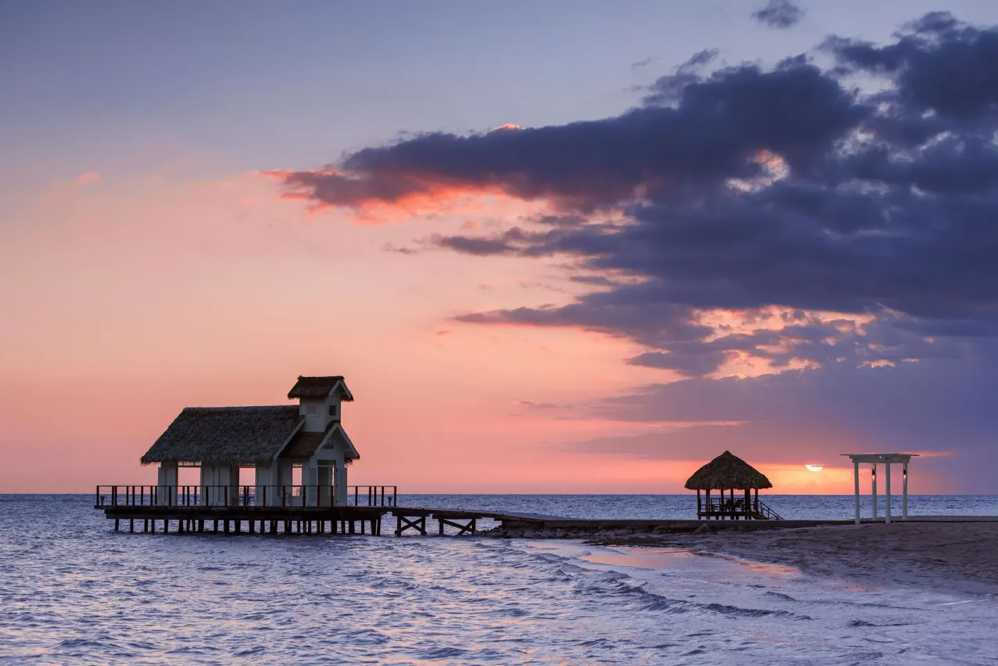 Overwater chapel and beach structures silhouetted at sunset at Sandals South Coast.