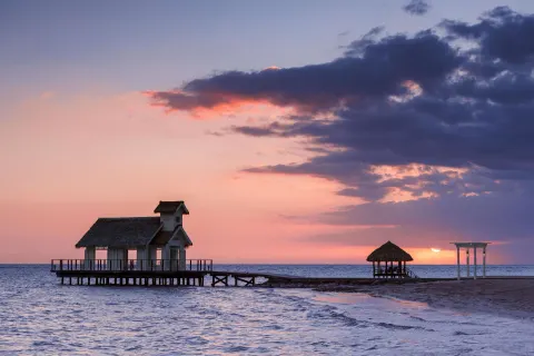 Overwater chapel and beach structures silhouetted at sunset at Sandals South Coast.