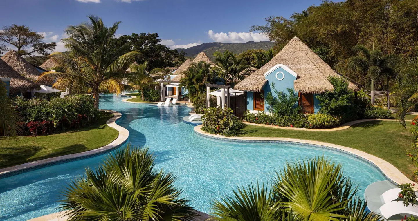 Curving swim-up pool with thatched villas and tropical gardens at Sandals South Coast.