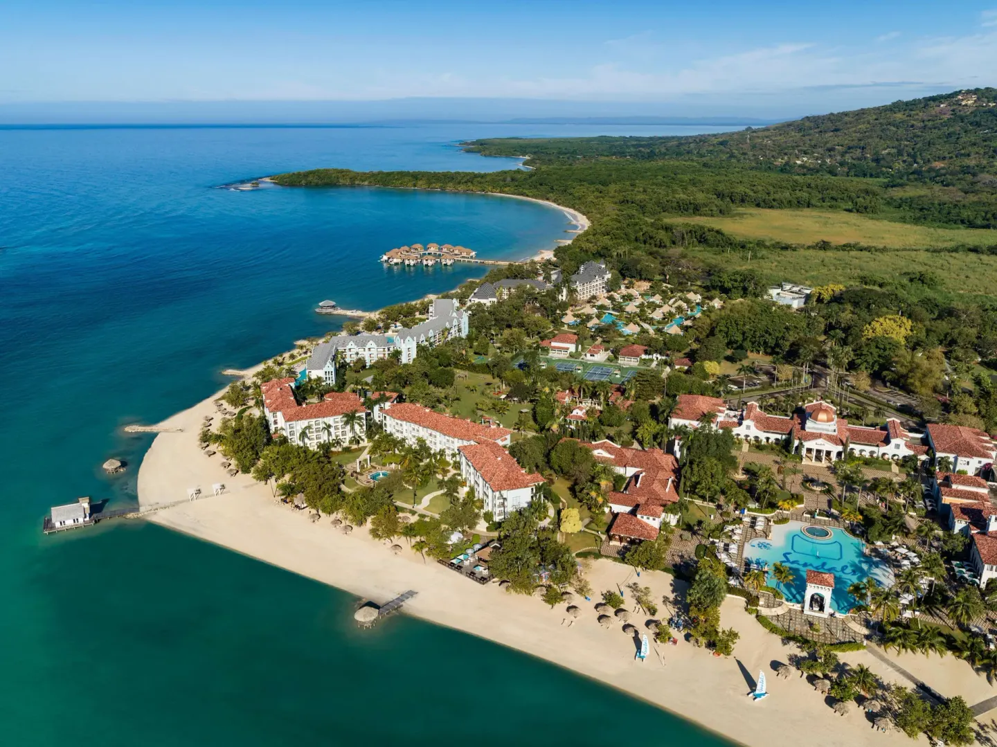 Wide aerial view of Sandals South Coast with beach, pools, and overwater bungalows.