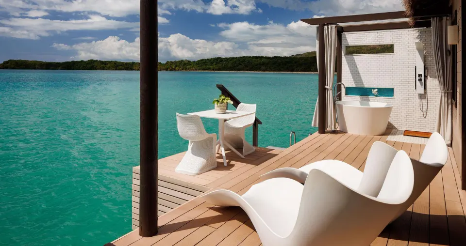 Overwater villa deck with loungers, dining table and outdoor tub at Sandals South Coast.