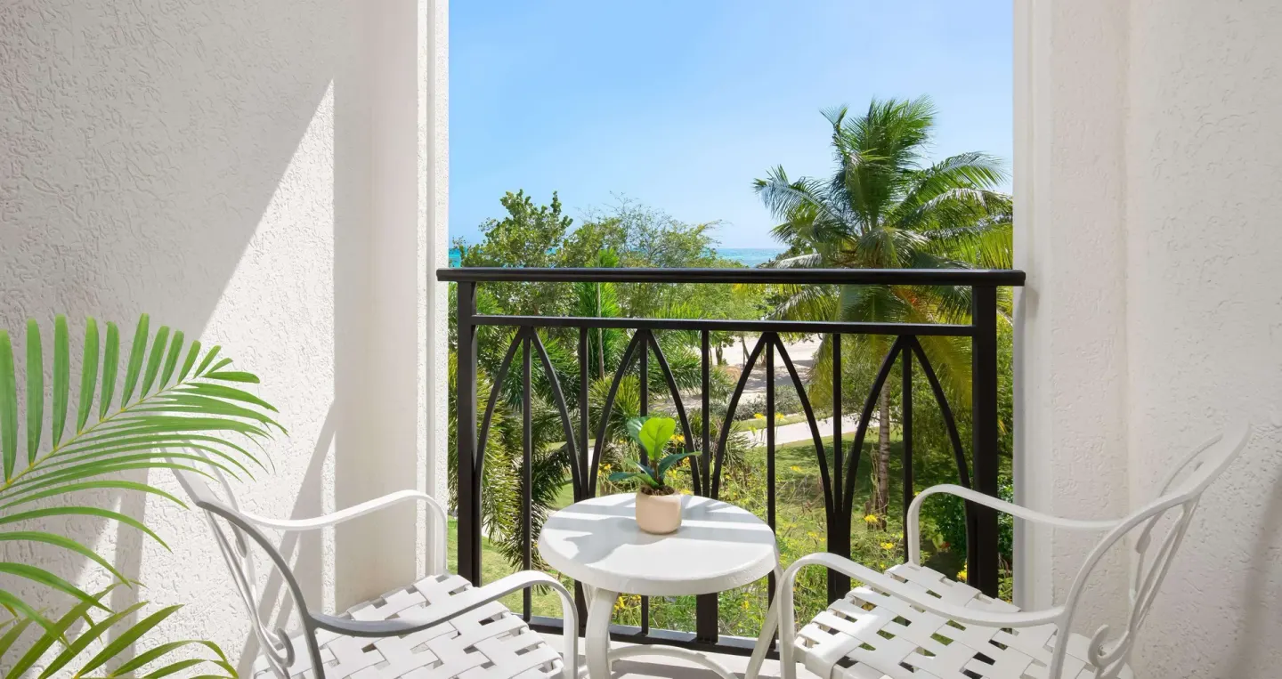 Balcony chairs overlooking gardens, palms, and ocean at Sandals South Coast.