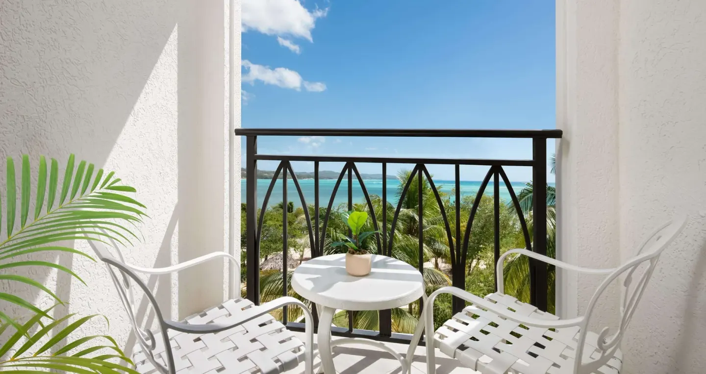 Balcony seating with turquoise ocean view from a honeymoon room at Sandals South Coast.
