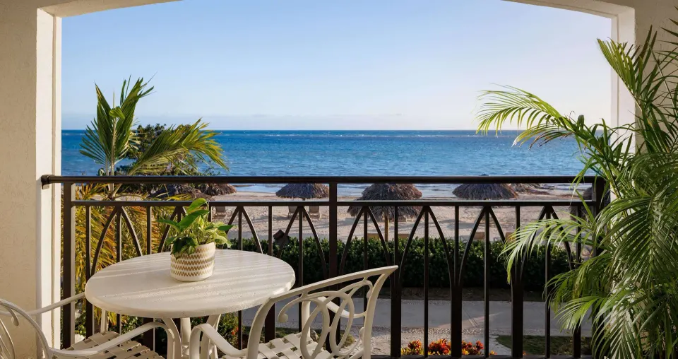 Furnished ocean-view balcony with table, chairs, and palms at Sandals South Coast.