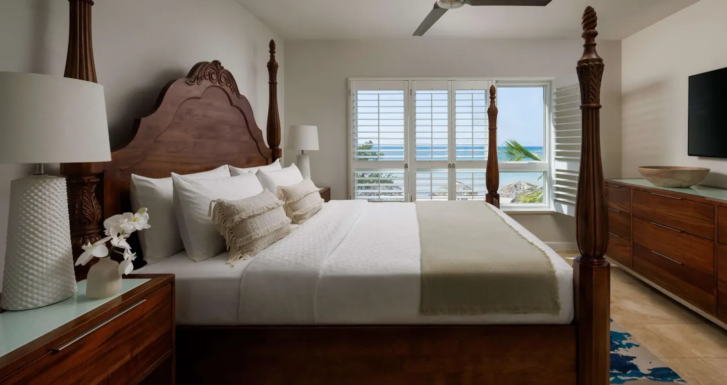 Four-poster king bed and ocean-facing shutters in a guest room at Sandals South Coast.