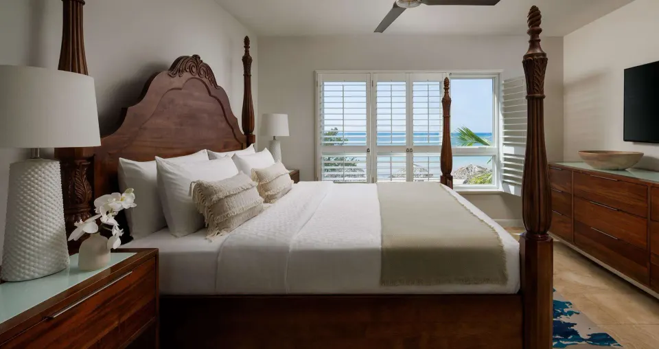 Four-poster king bed and ocean-facing shutters in a guest room at Sandals South Coast.