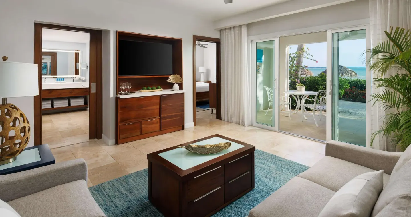Ocean-view living area with sofas, patio doors, and bathroom doorway at Sandals South Coast.