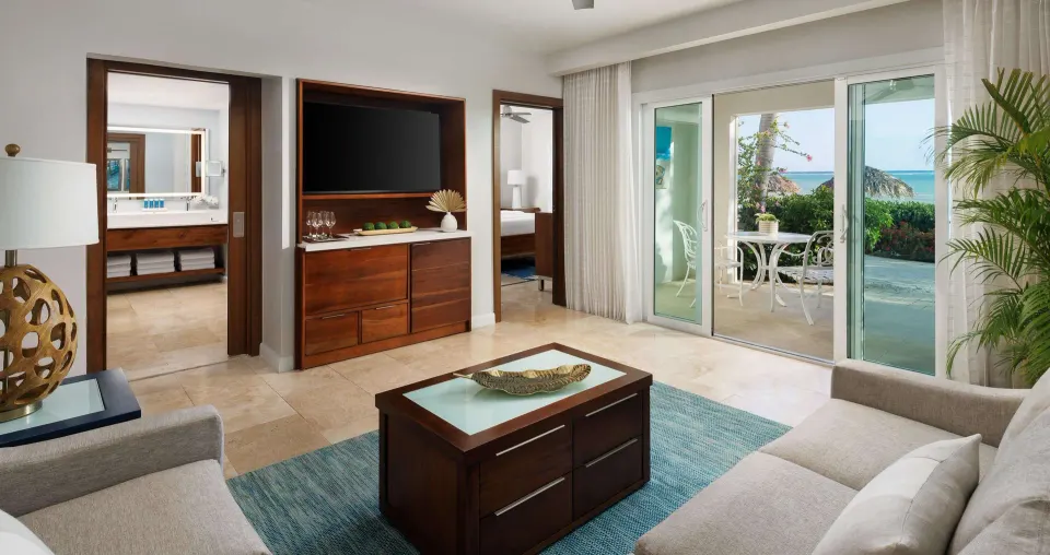 Ocean-view living area with sofas, patio doors, and bathroom doorway at Sandals South Coast.