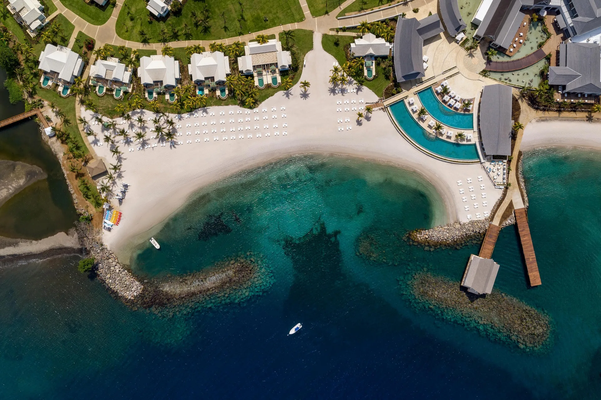 Top-down aerial of the beach, pools, villas, and pier at Sandals St. Vincent and the Grenadines.