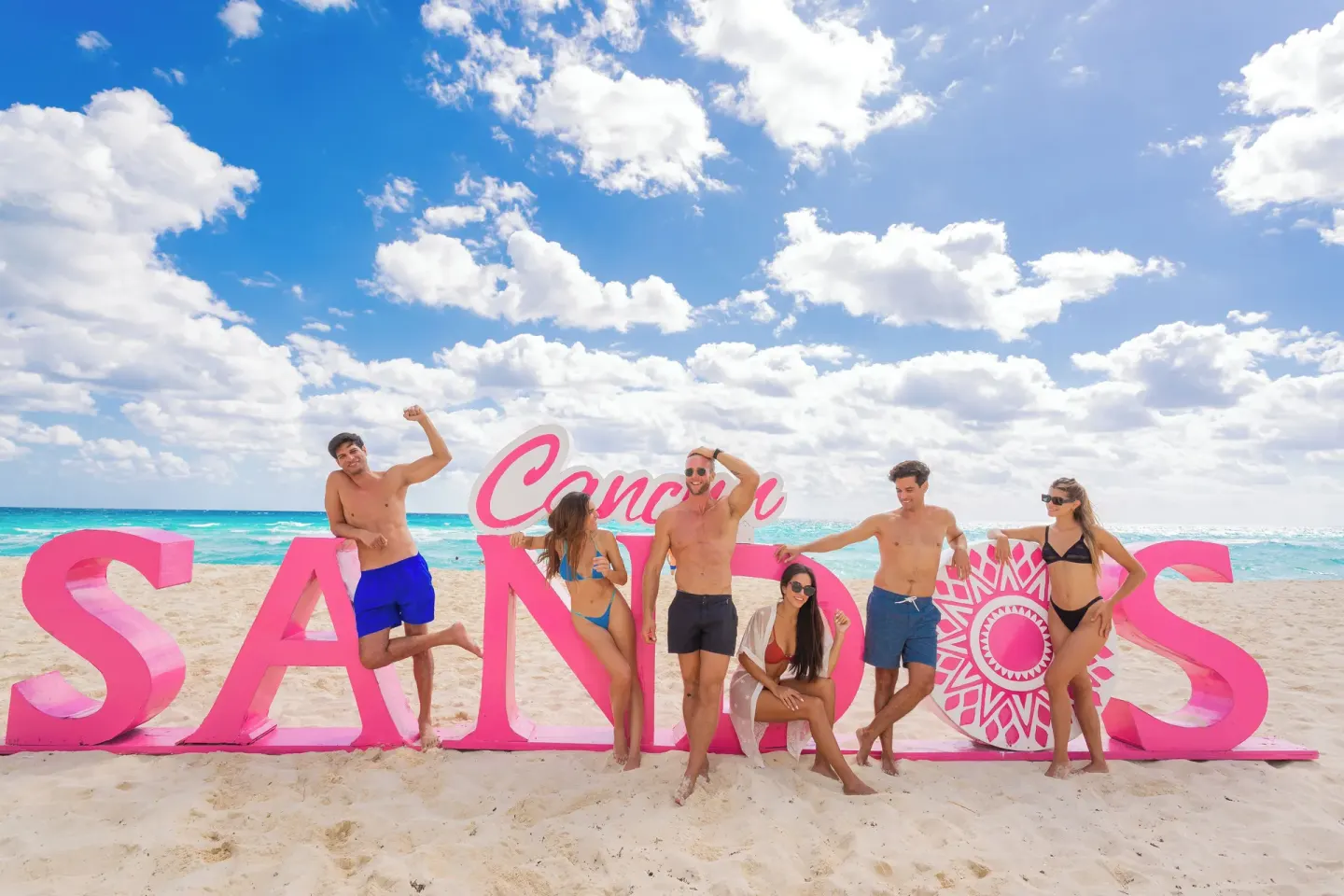 Group posing beside a large pink Sandos beach sign at Sandos Cancún.