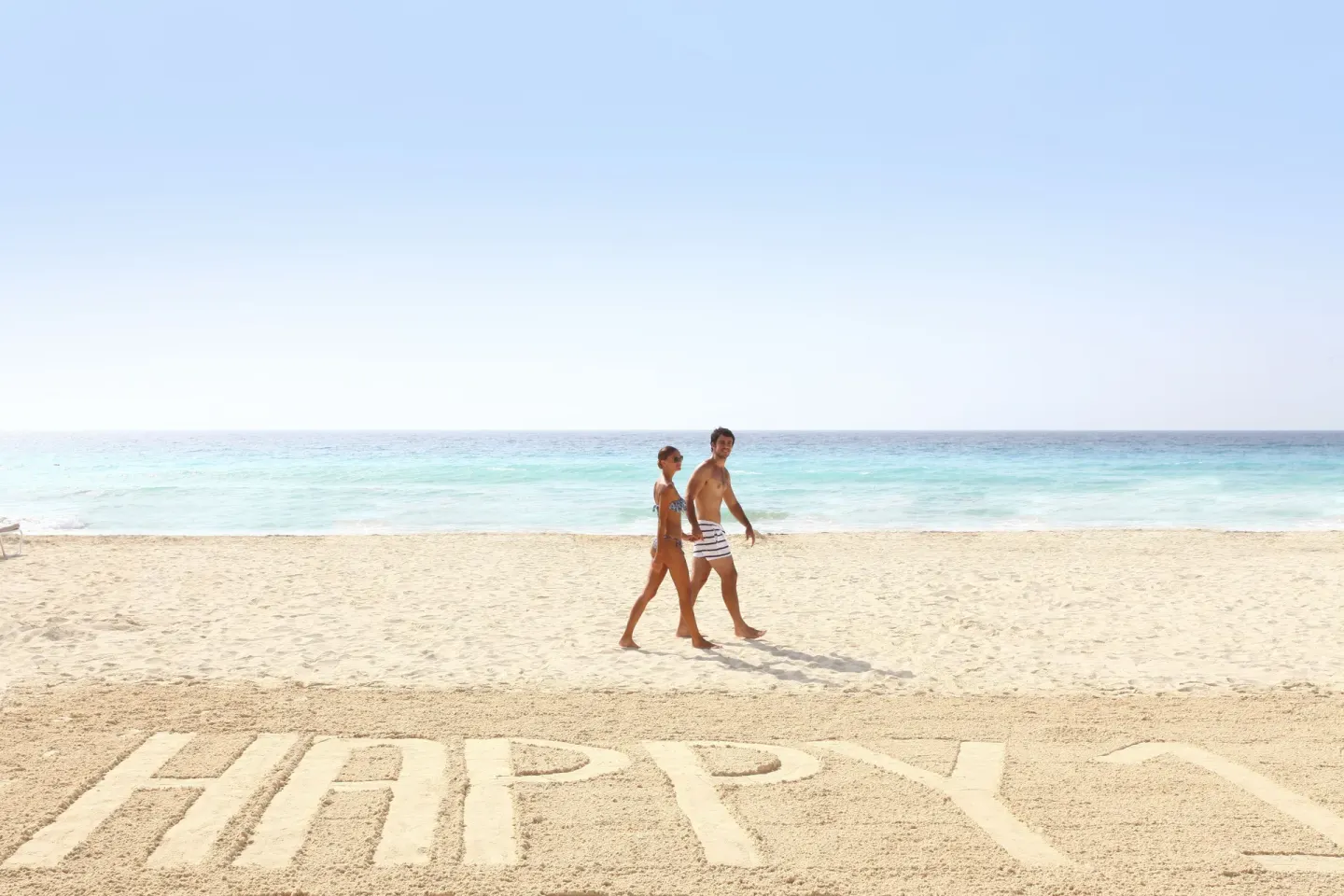 Couple walking on the sandy beach by turquoise water at Sandos Cancún.
