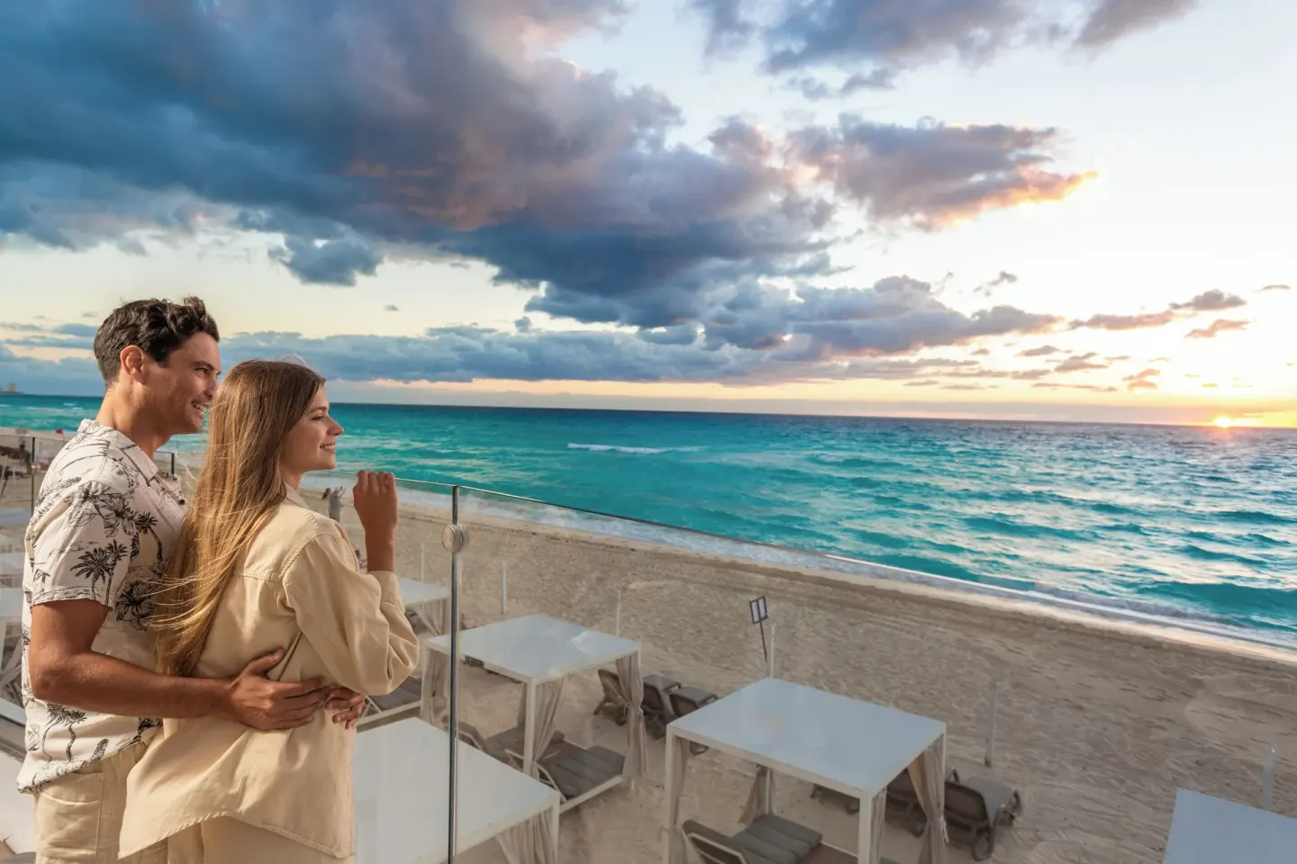 A couple watches the Caribbean sunset from a beachfront terrace at Sandos Cancún.
