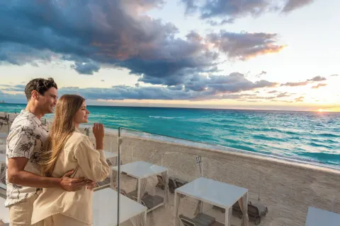 A couple watches the Caribbean sunset from a beachfront terrace at Sandos Cancún.