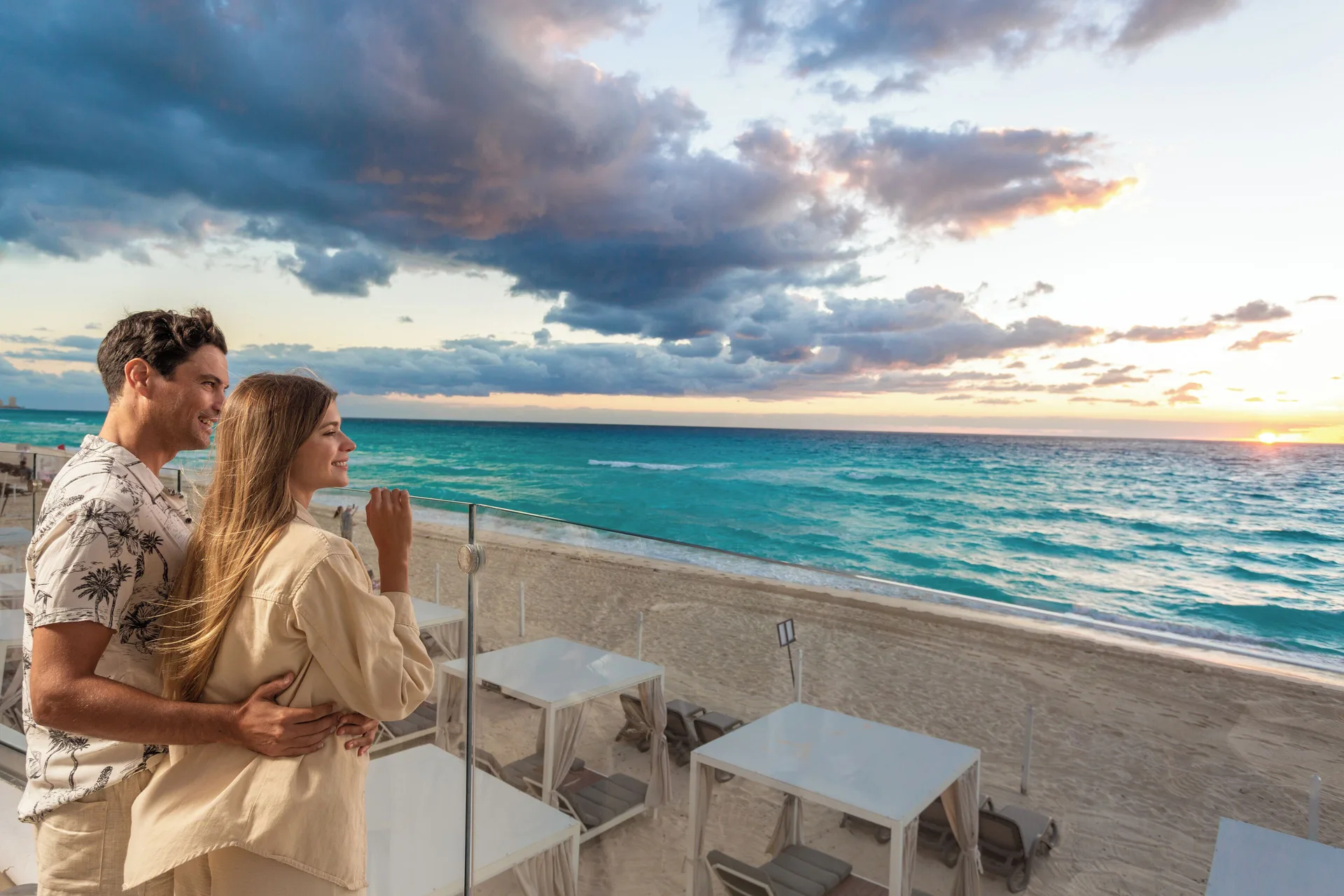 A couple watches the Caribbean sunset from a beachfront terrace at Sandos Cancún.