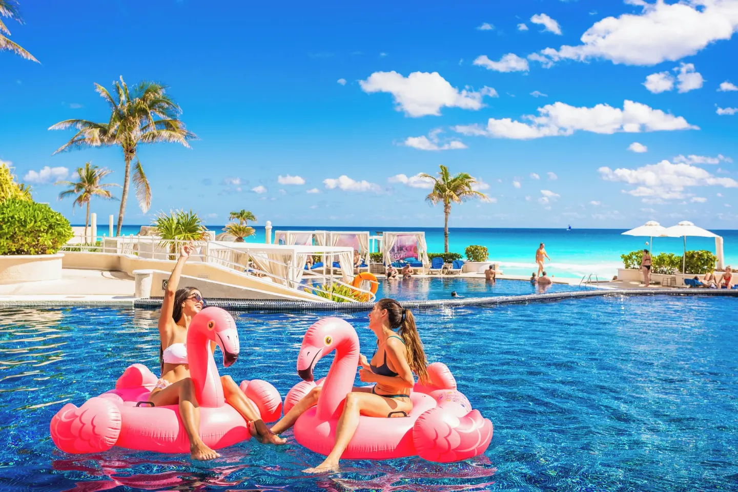 Guests on pink flamingo floats in the oceanfront pool at Sandos Cancún.