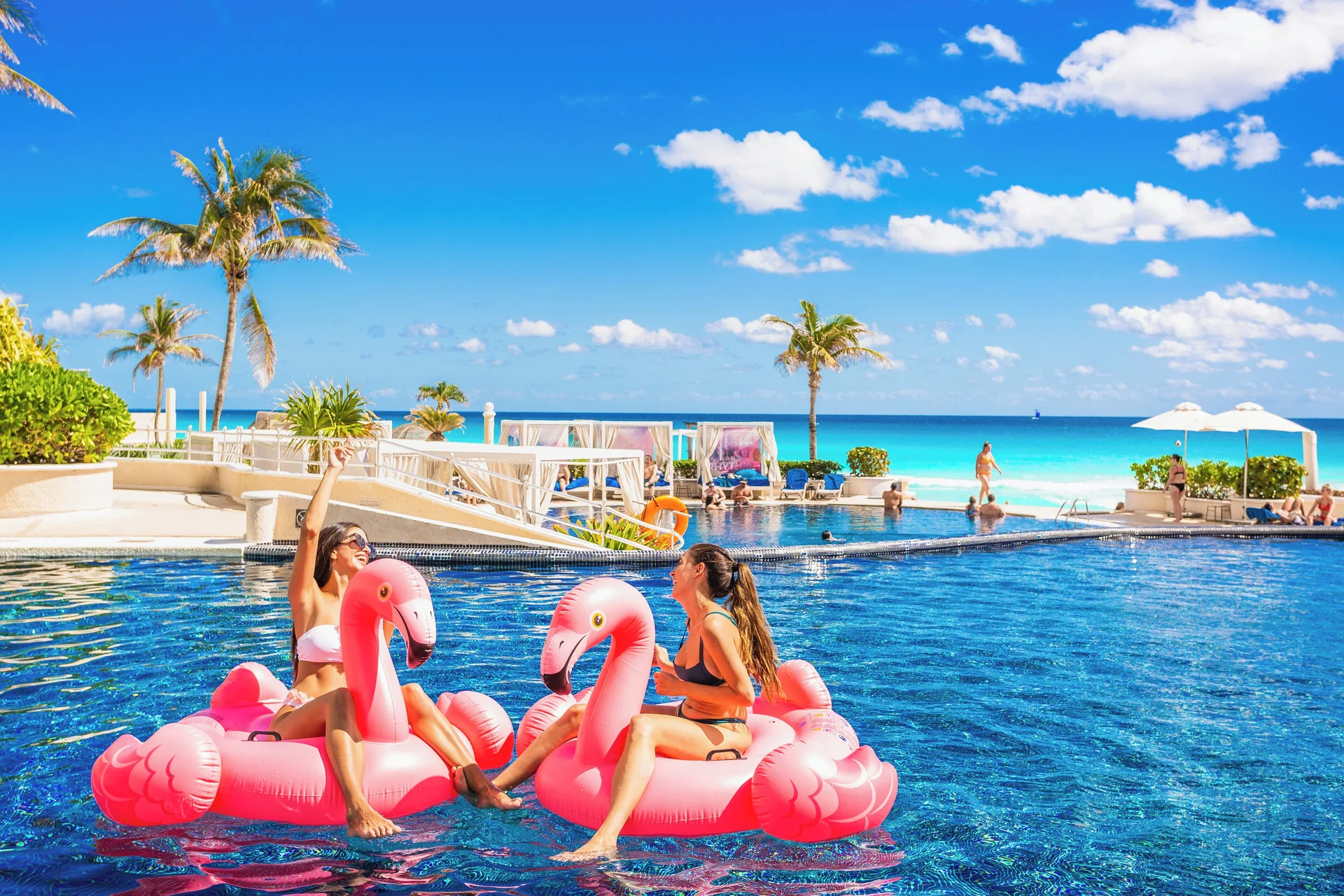 Guests on pink flamingo floats in the oceanfront pool at Sandos Cancún.