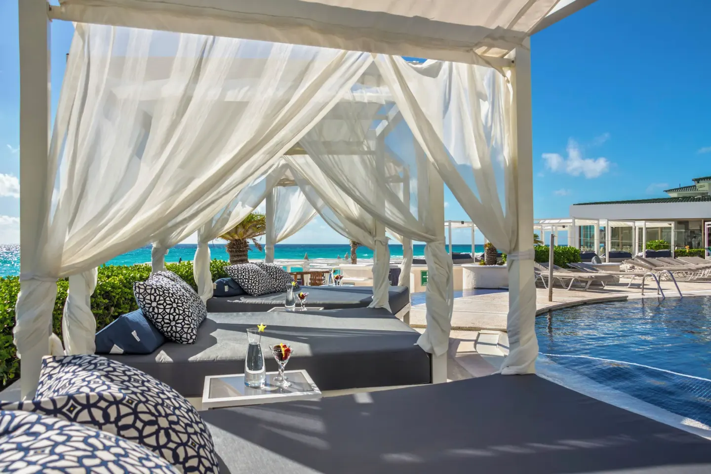 White curtained cabanas and loungers beside the pool at Sandos Cancún.
