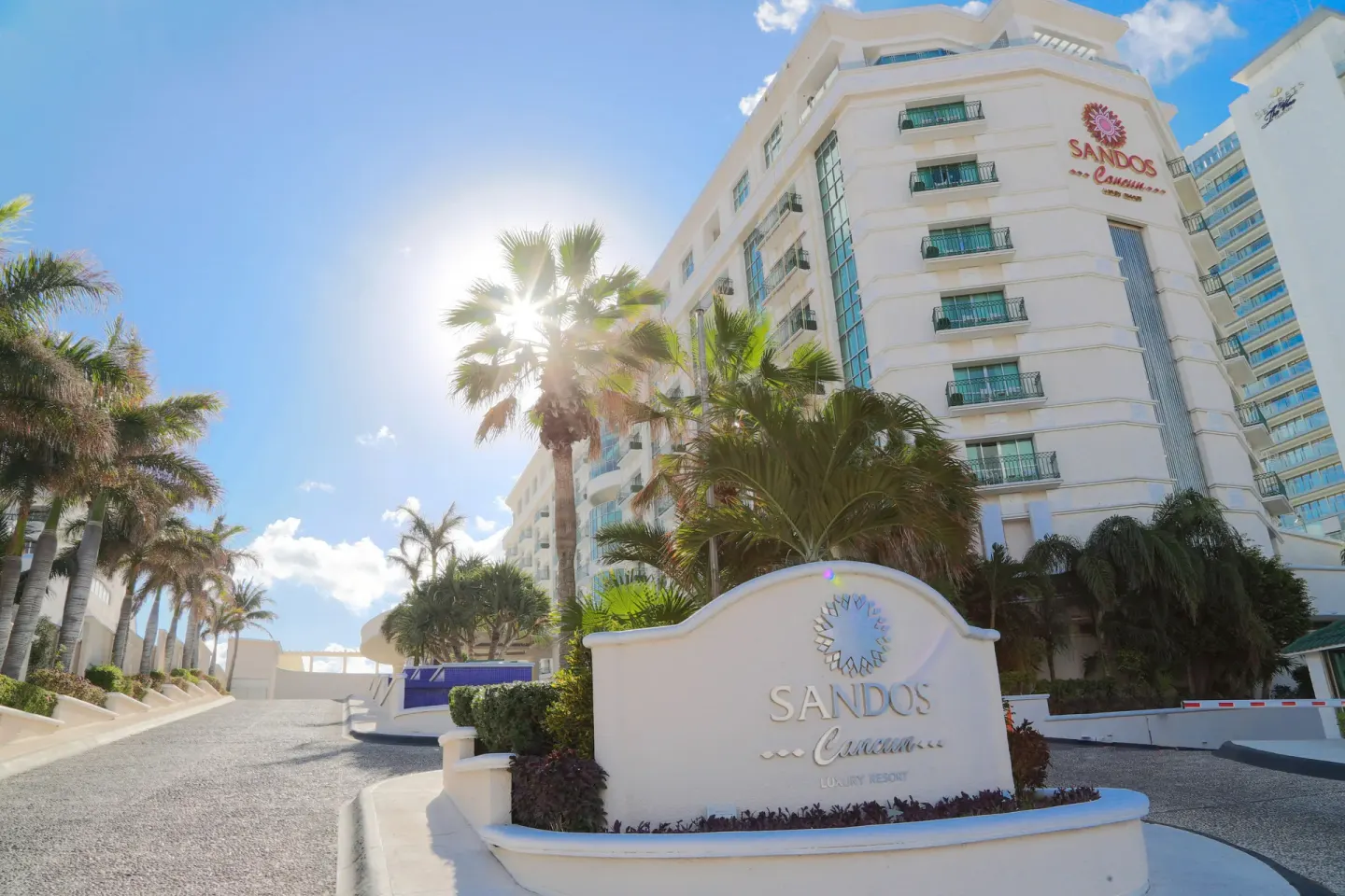 Sandos Cancún entrance sign and resort tower framed by palm trees.