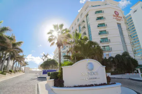 Sandos Cancún entrance sign and resort tower framed by palm trees.