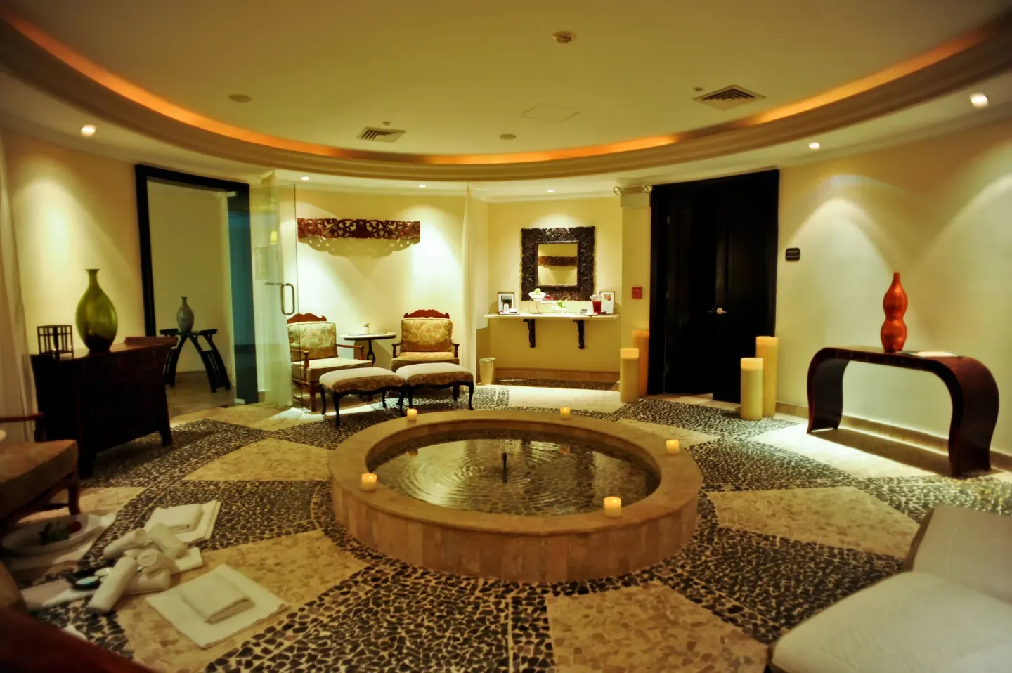 A spa relaxation room with a round water feature and candles at Sandos Cancún.