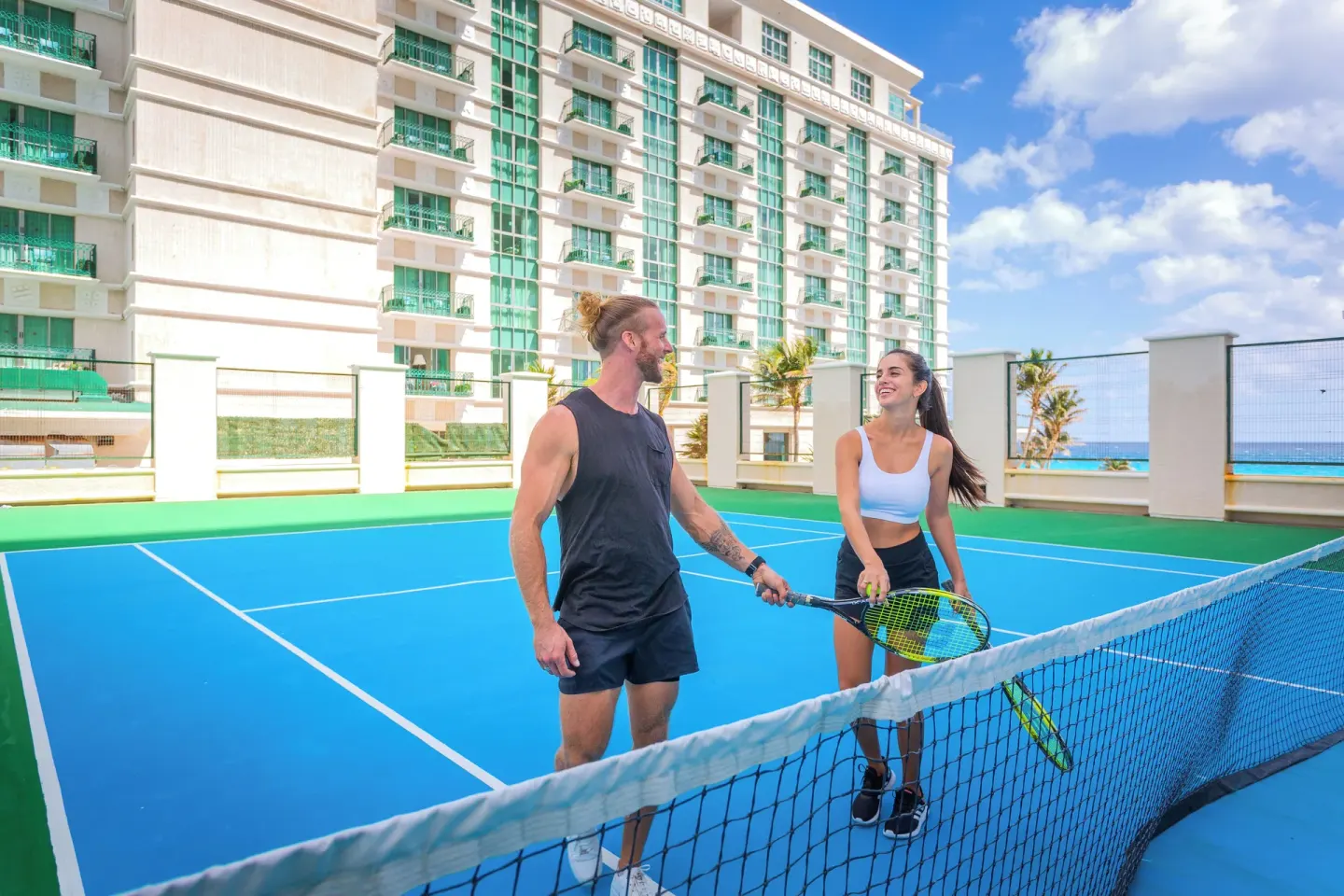 Two guests with rackets at the tennis net at Sandos Cancún.