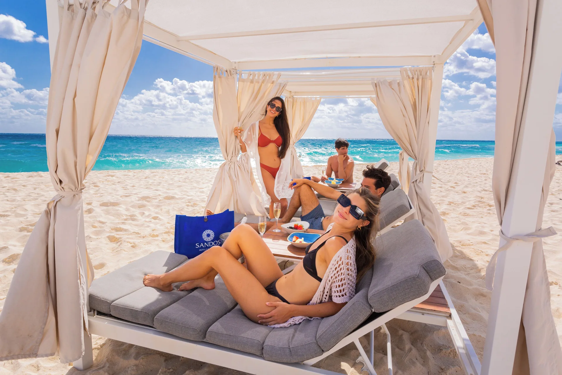 Guests reclining in a white beach cabana with ocean views at Sandos Cancún.