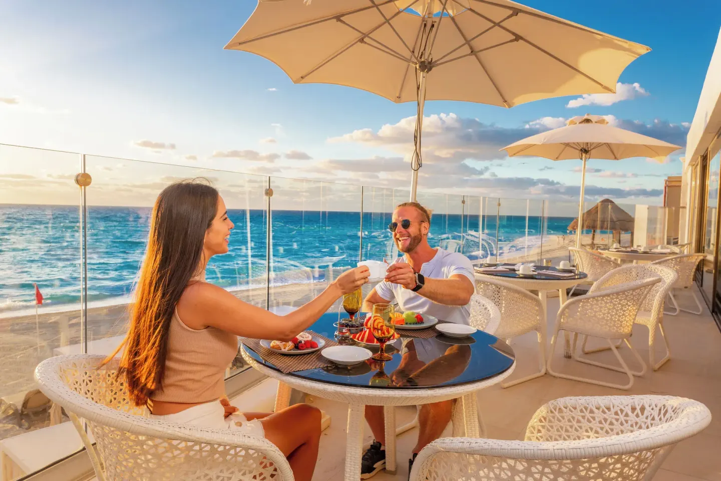 Two guests toast at an oceanfront terrace table at Sandos Cancún.