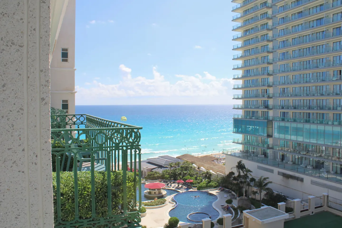 Deluxe Room balcony view of the ocean, pool, and neighboring tower at Sandos Cancún.