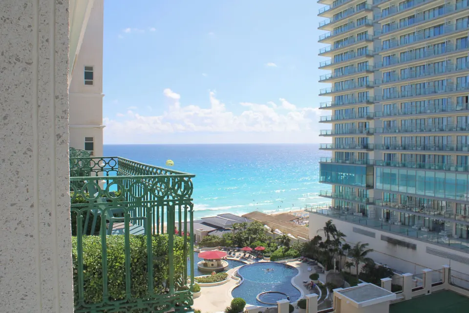 Deluxe Room balcony view of the ocean, pool, and neighboring tower at Sandos Cancún.