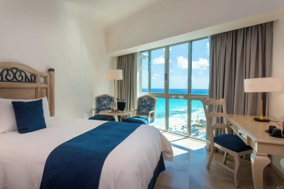 Deluxe Room king bed, desk, and ocean view windows at Sandos Cancún.