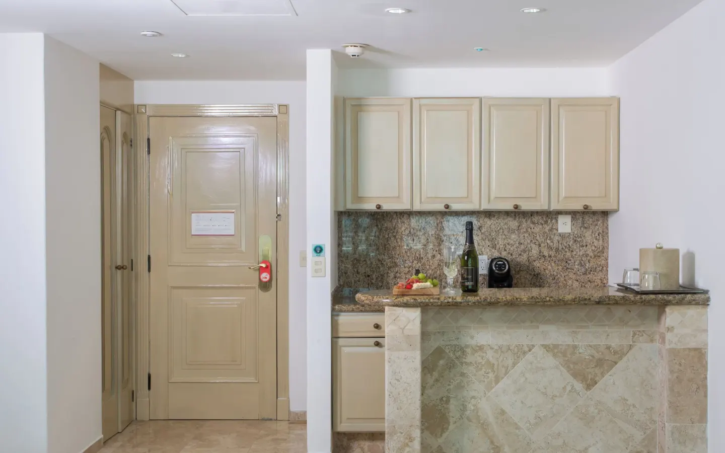 Laguna Suite entry area with kitchenette, cabinets, granite counter, and door at Sandos Cancún.