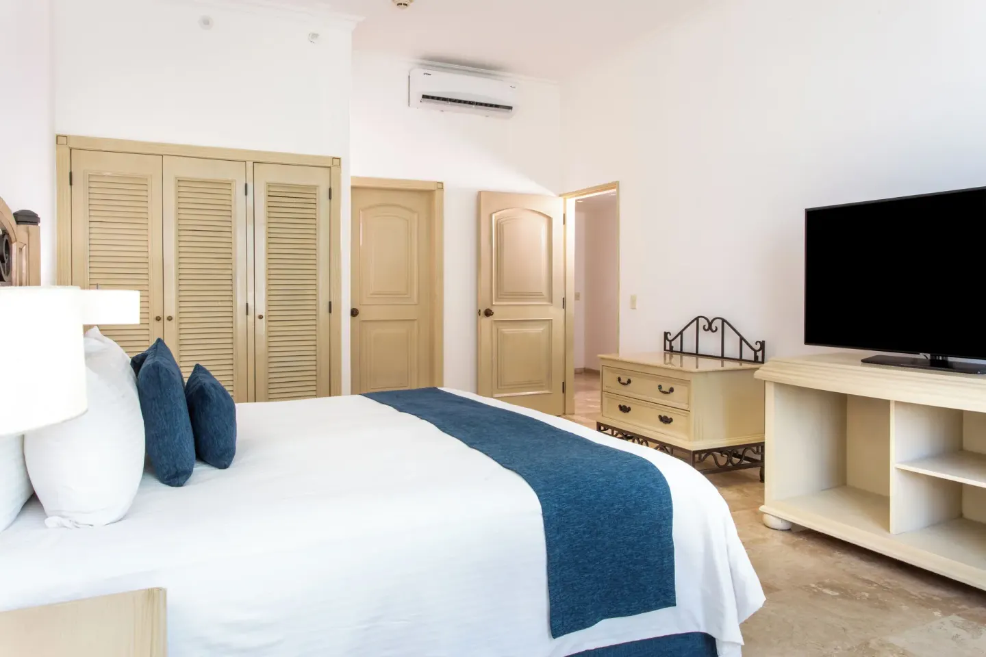 Laguna Suite bedroom with king bed, TV, closet doors, and dresser at Sandos Cancún.