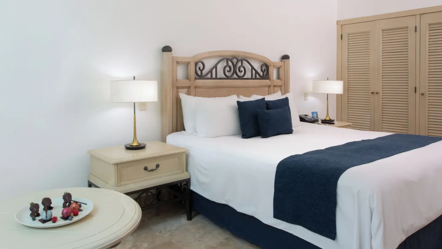 Laguna Suite king bed with nightstands, lamps, closet doors, and a small table at Sandos Cancún.