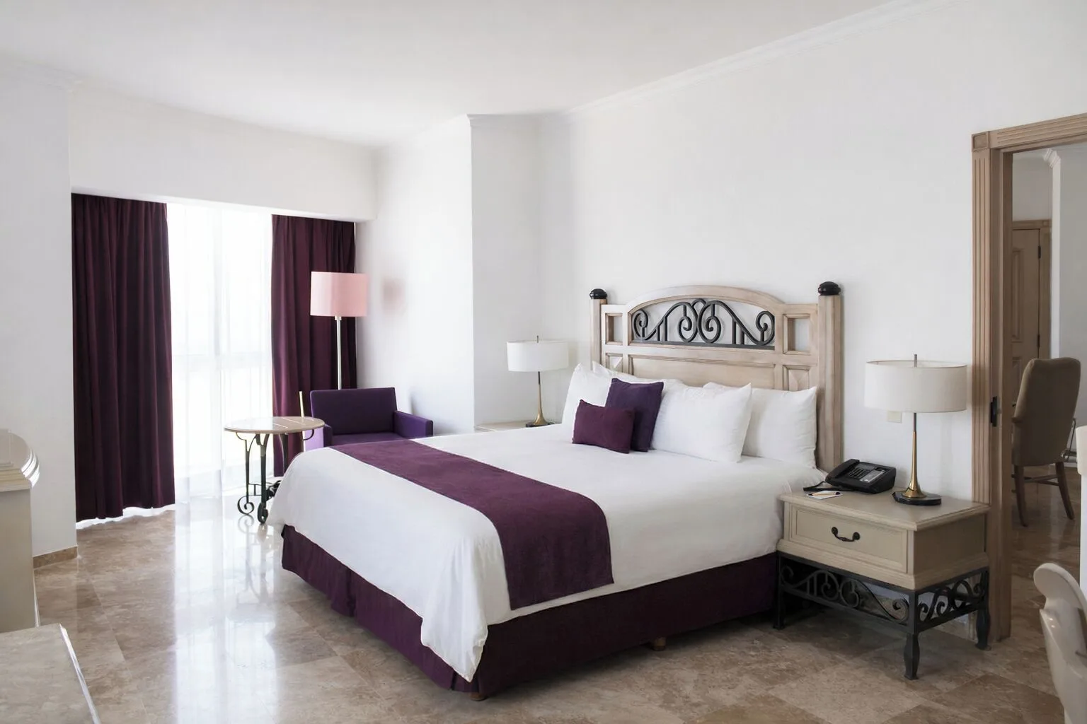 Laguna Suite bedroom with king bed, purple accents, chair, table, and window at Sandos Cancún.