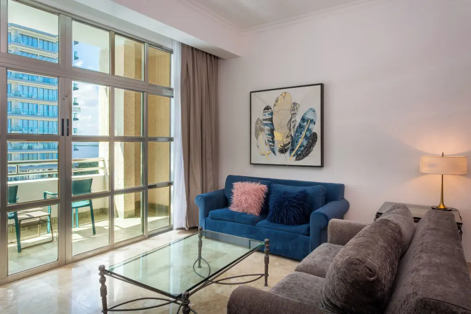 Laguna Suite living room with sofas, glass coffee table, balcony doors, and partial view at Sandos Cancún.