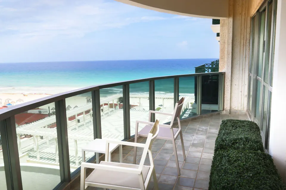 Sandos Cancún balcony with chairs, side tables, glass railing, and ocean view at Sandos Cancún.