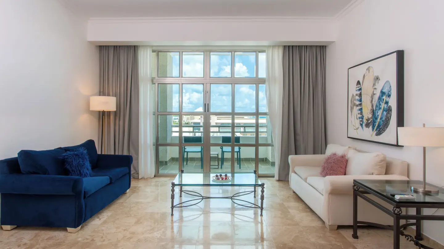 Sandos Cancún living room with blue and white sofas, glass table, and balcony doors at Sandos Cancún.
