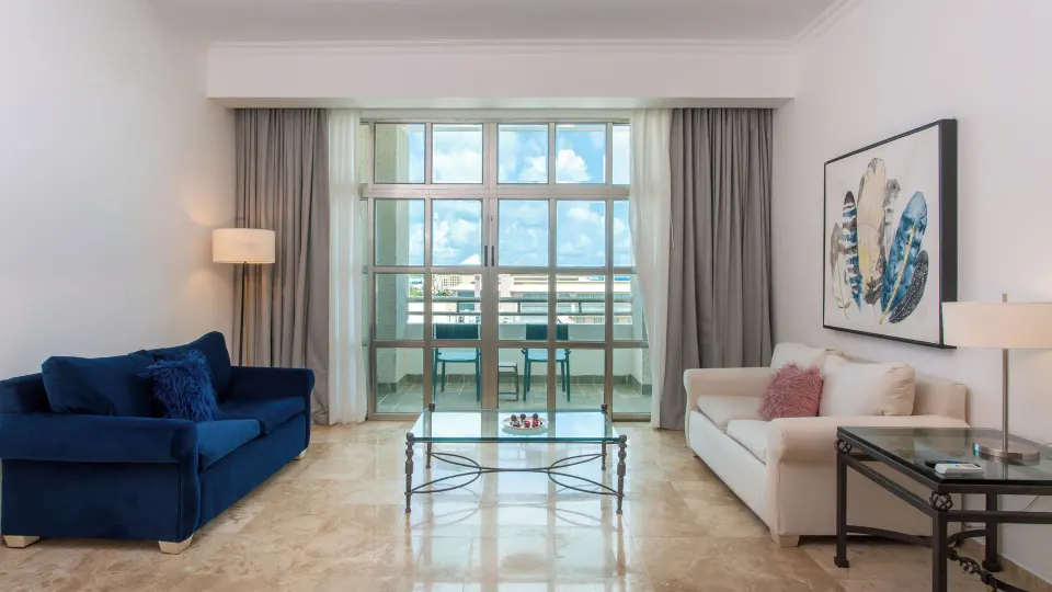 Sandos Cancún living room with blue and white sofas, glass table, and balcony doors at Sandos Cancún.