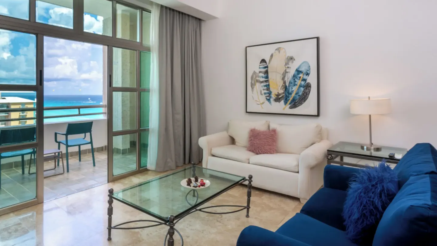 Sandos Cancún sitting area with sofas, glass coffee table, balcony, and ocean view at Sandos Cancún.