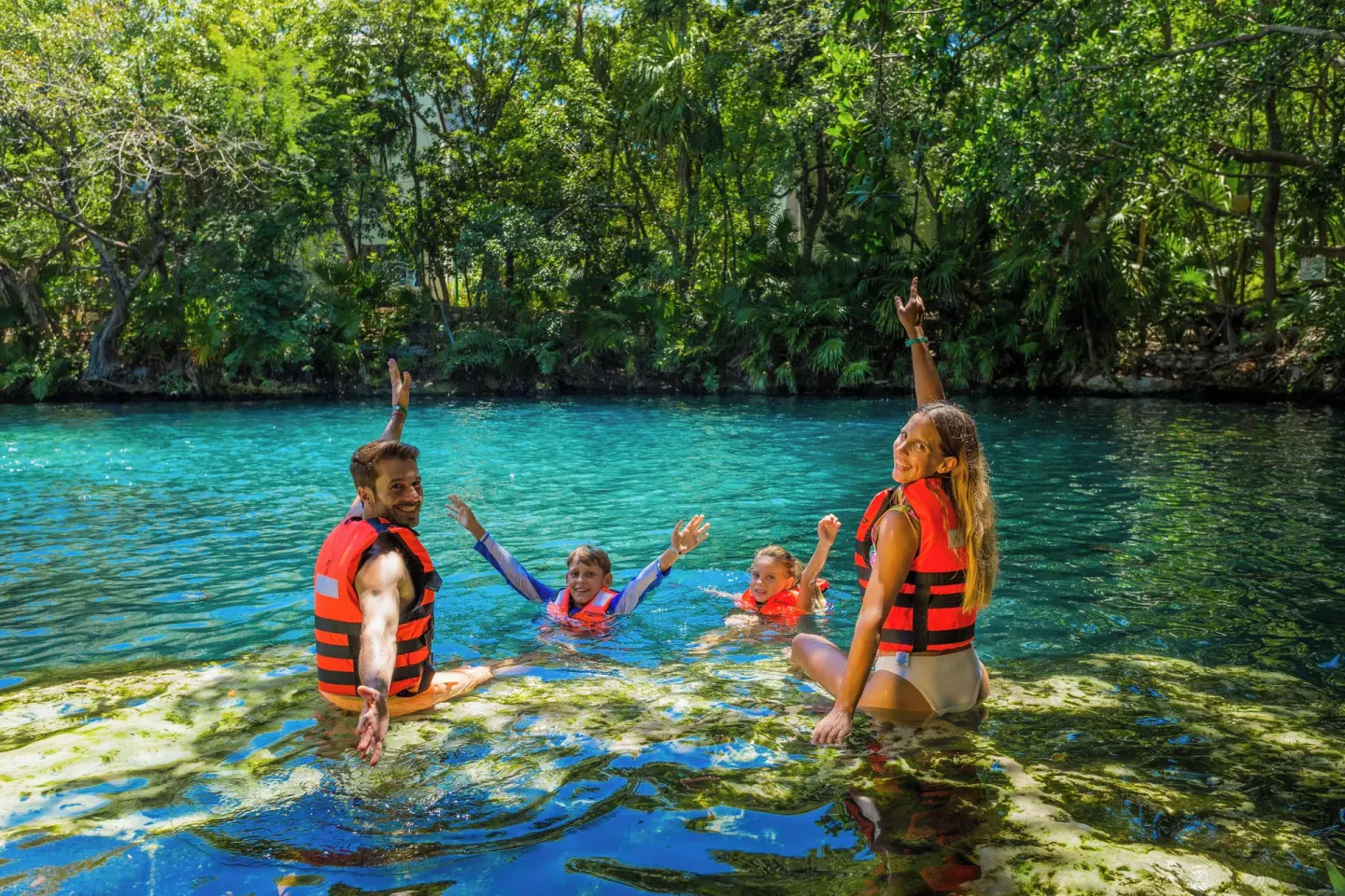 Family swimming in a clear cenote at Sandos Caracol Nature Resort & Water Park.