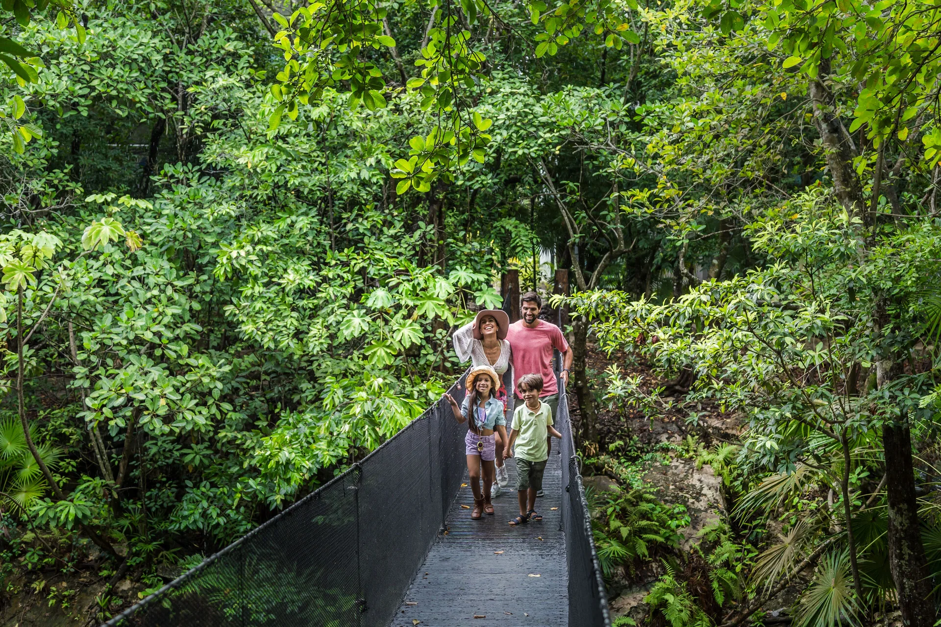 Family walking on a jungle suspension bridge at Sandos Caracol Nature Resort & Water Park.