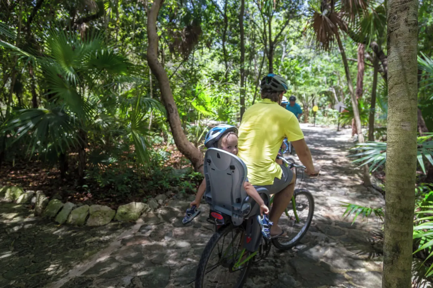 Adult cycling with a child seat on a jungle trail at Sandos Caracol Nature Resort & Water Park.