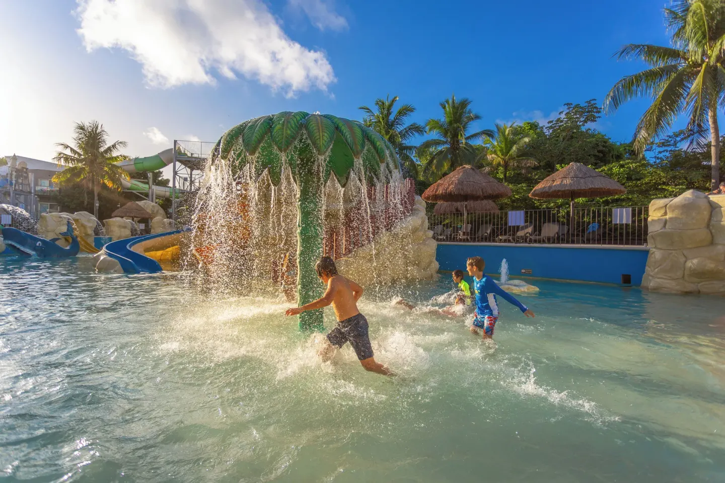 Children splash under a palm-shaped water feature at Sandos Caracol Nature Resort & Water Park.
