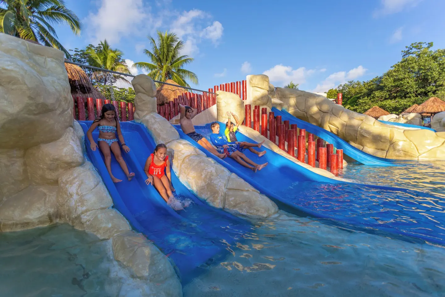 Children ride side-by-side blue pool slides at Sandos Caracol Nature Resort & Water Park.