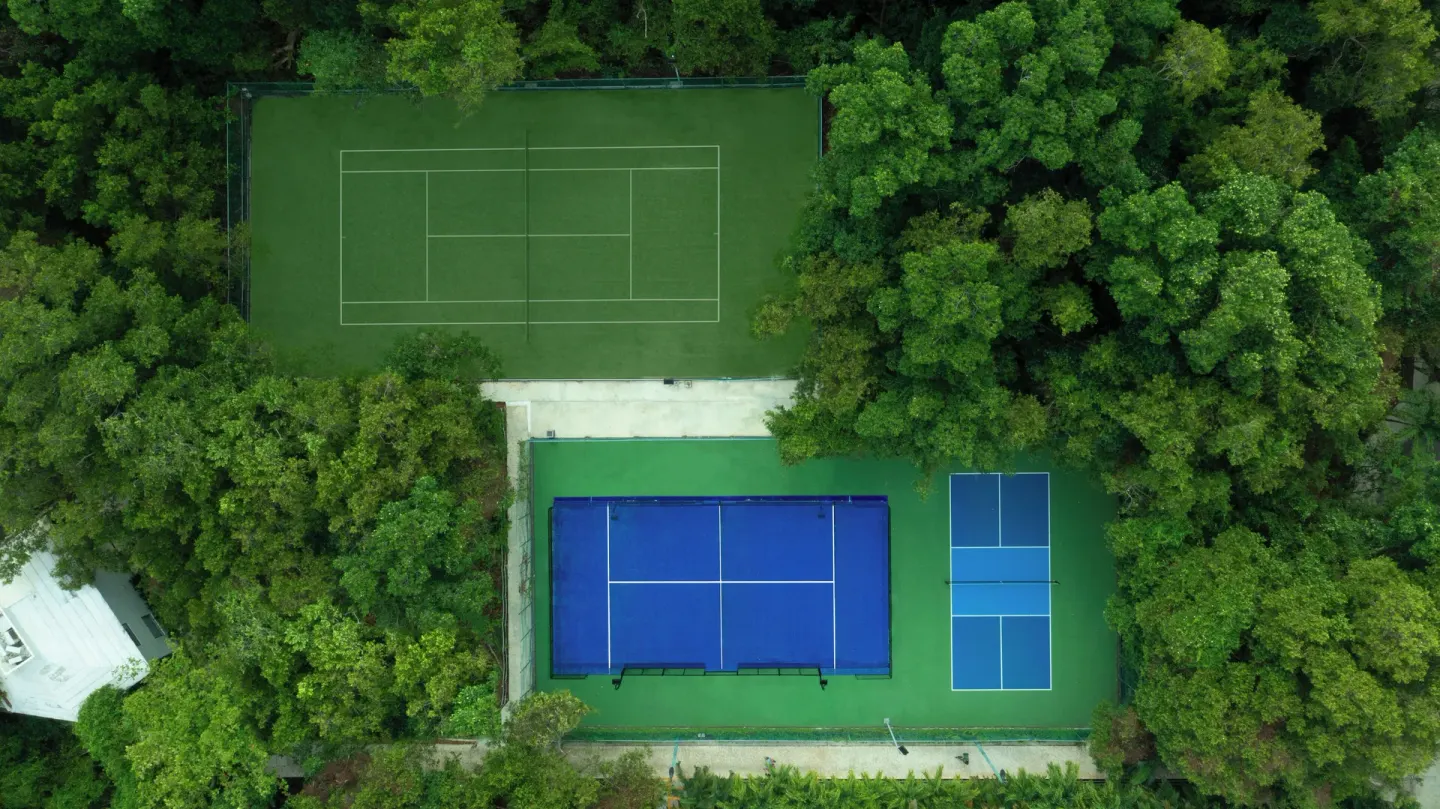Aerial view of sports courts surrounded by forest at Sandos Caracol Nature Resort & Water Park.