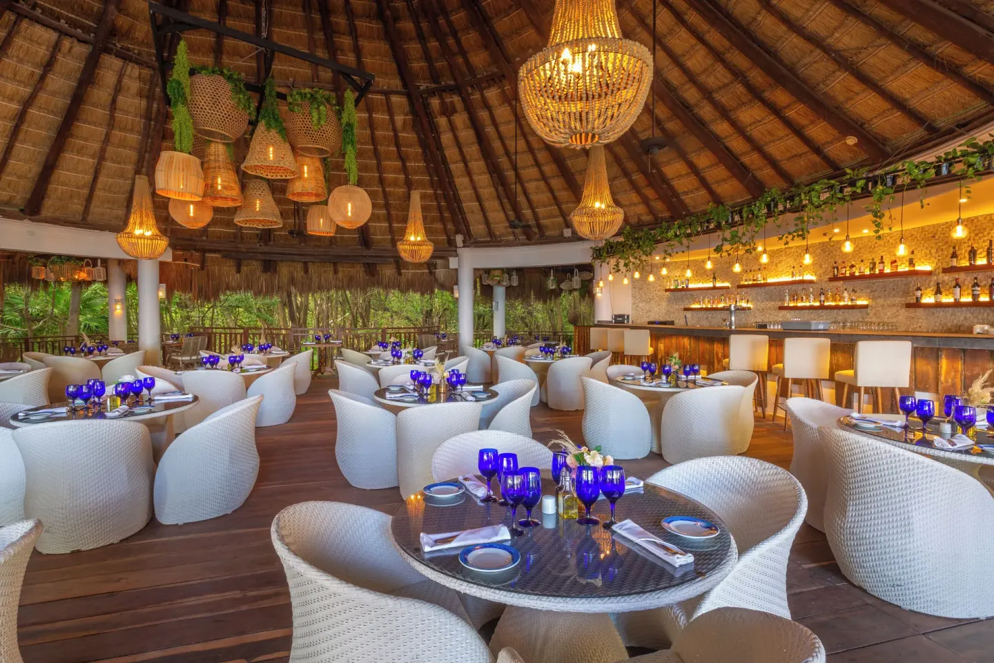 A thatched-roof dining room with a bar and blue glassware at Sandos Caracol Nature Resort & Water Park.