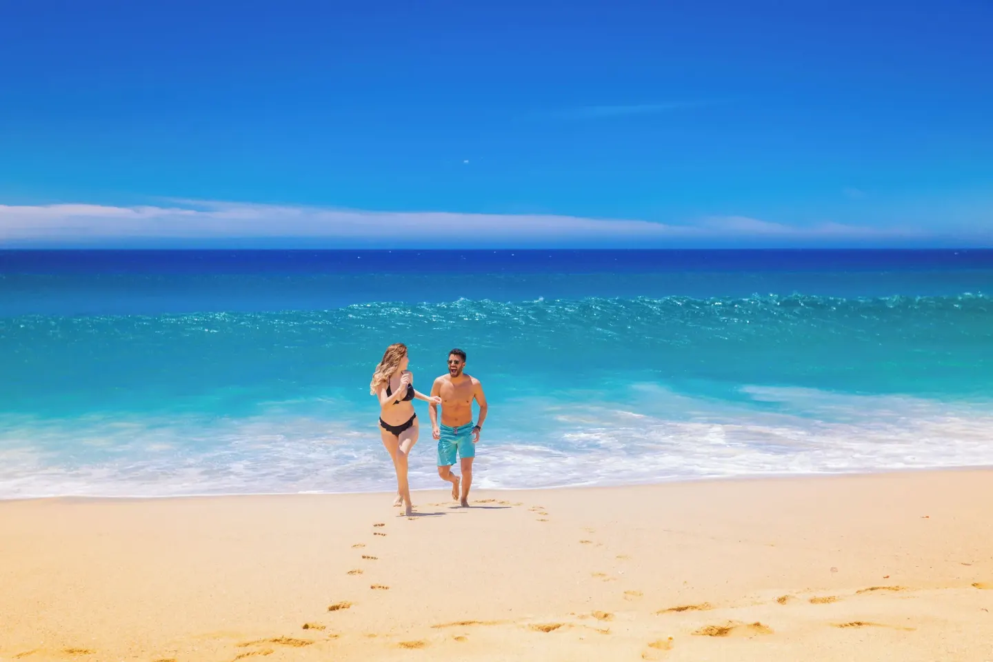 A couple runs from the surf across the sandy beach at Sandos Finisterra.